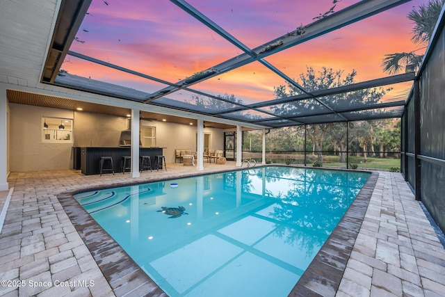 pool at dusk featuring a patio area, glass enclosure, and exterior bar