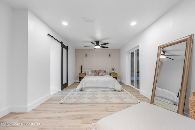 bedroom featuring ceiling fan, a barn door, light hardwood / wood-style floors, and two closets