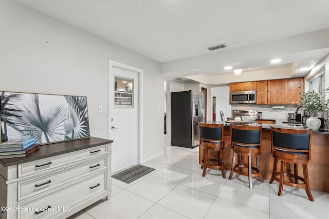 kitchen with light tile patterned floors, white cabinetry, stainless steel appliances, a kitchen bar, and decorative backsplash