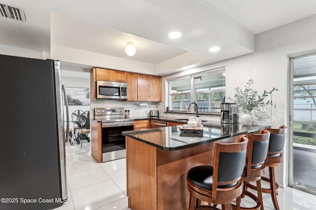 kitchen with sink, dark stone countertops, appliances with stainless steel finishes, kitchen peninsula, and backsplash