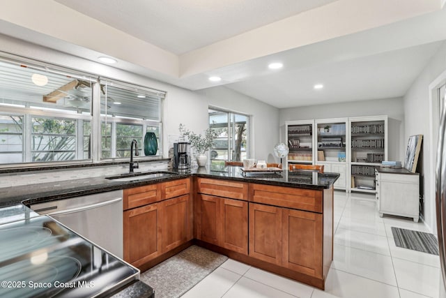 kitchen with sink, dark stone counters, stainless steel dishwasher, light tile patterned floors, and kitchen peninsula