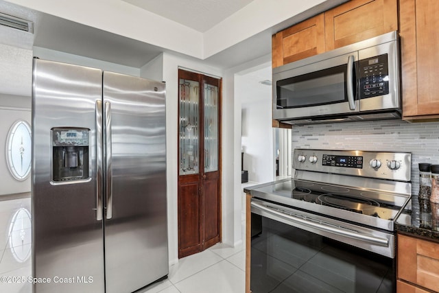 kitchen featuring light tile patterned flooring, appliances with stainless steel finishes, dark stone countertops, and backsplash