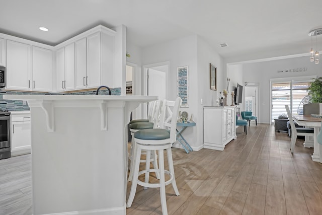 kitchen featuring stainless steel appliances, light wood-type flooring, white cabinets, and a kitchen bar