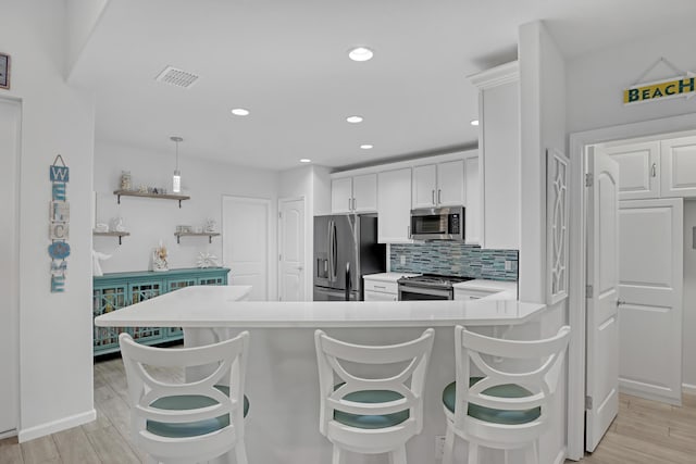 kitchen with appliances with stainless steel finishes, decorative light fixtures, a breakfast bar, and white cabinets