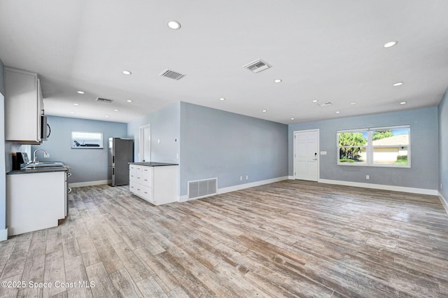 unfurnished living room featuring plenty of natural light, sink, and light hardwood / wood-style floors