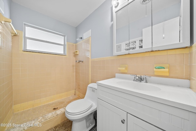 bathroom with tiled shower, vanity, toilet, and tile walls