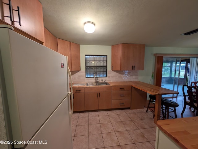 kitchen with sink, a textured ceiling, light tile patterned floors, white refrigerator, and backsplash