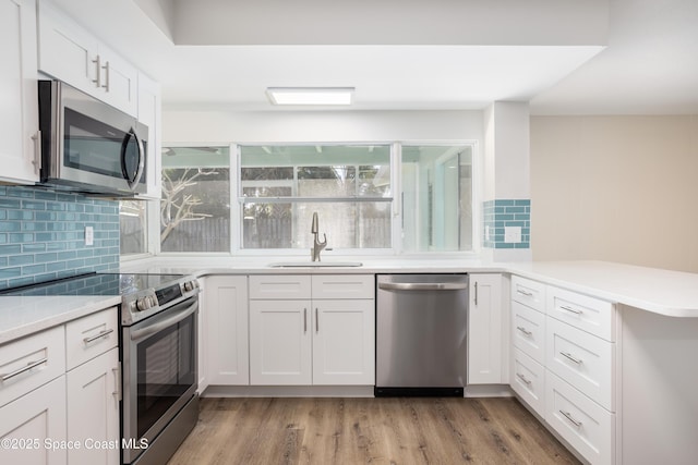 kitchen with white cabinetry, kitchen peninsula, light hardwood / wood-style flooring, sink, and appliances with stainless steel finishes