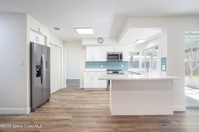 kitchen featuring white cabinetry, light hardwood / wood-style flooring, sink, backsplash, and appliances with stainless steel finishes