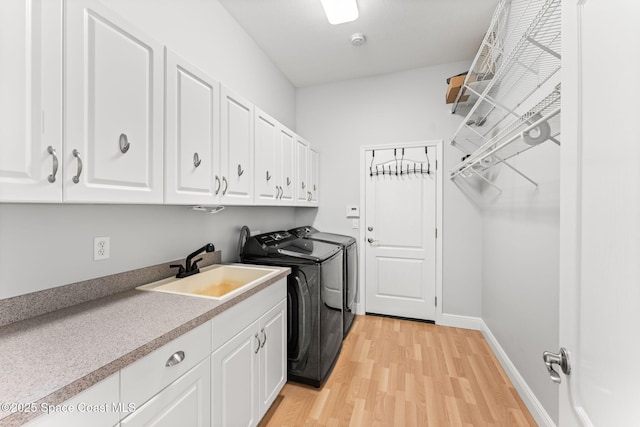 clothes washing area with cabinets, sink, independent washer and dryer, and light hardwood / wood-style floors