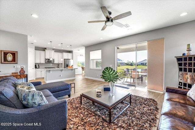 living room featuring ceiling fan, a textured ceiling, and light wood-type flooring