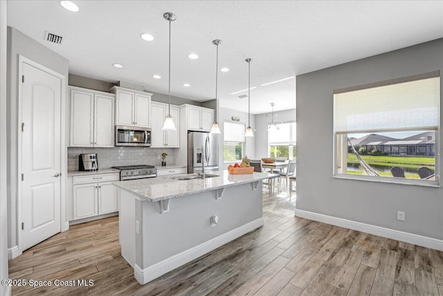 kitchen with white cabinetry, appliances with stainless steel finishes, an island with sink, and pendant lighting