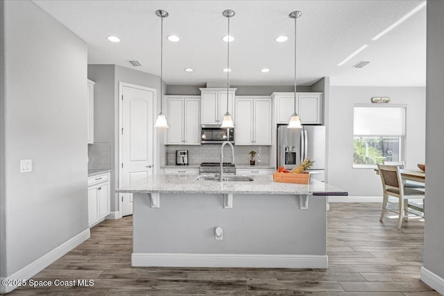 kitchen featuring pendant lighting, stainless steel appliances, a kitchen island with sink, and sink