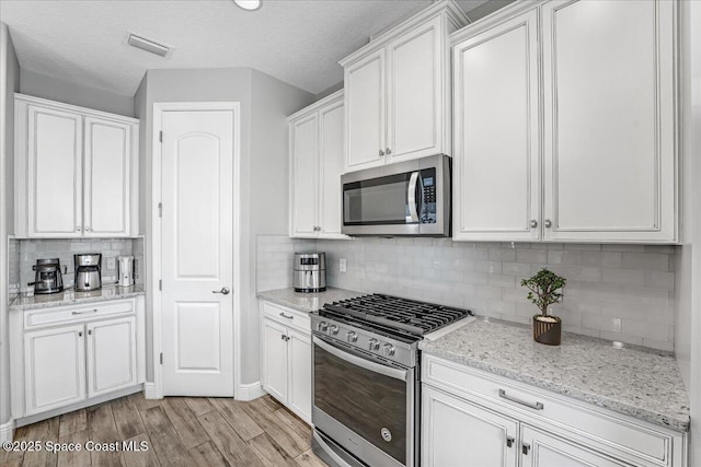 kitchen with appliances with stainless steel finishes, white cabinetry, backsplash, light hardwood / wood-style floors, and light stone countertops