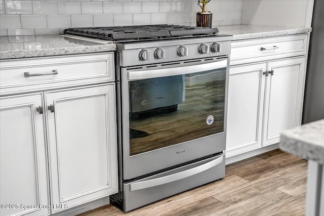 kitchen with white cabinetry, backsplash, gas range, and light hardwood / wood-style flooring