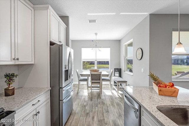 kitchen with decorative light fixtures, white cabinetry, light stone counters, stainless steel appliances, and light wood-type flooring