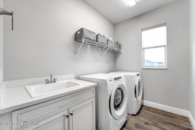 laundry area featuring sink, wood-type flooring, washing machine and dryer, and cabinets