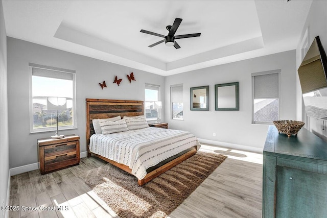 bedroom with a raised ceiling, ceiling fan, and light wood-type flooring