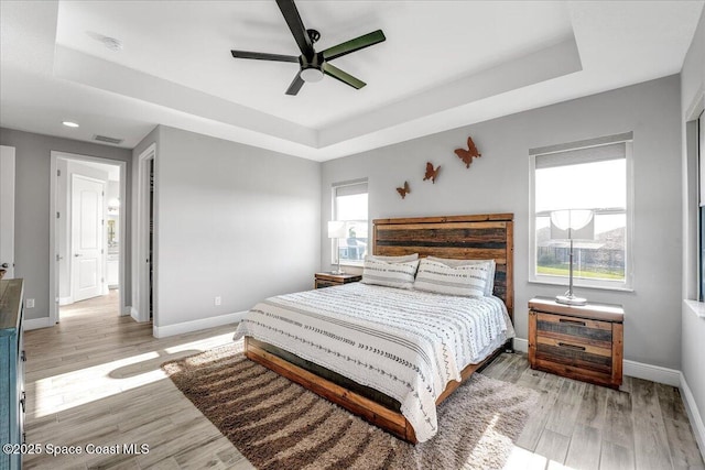 bedroom with ceiling fan, a tray ceiling, and light hardwood / wood-style floors