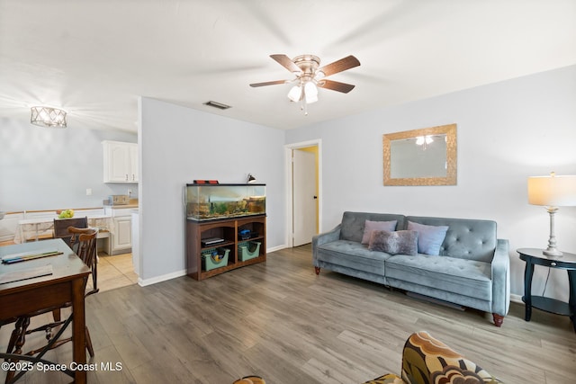 living room featuring baseboards, light wood-style flooring, visible vents, and a ceiling fan