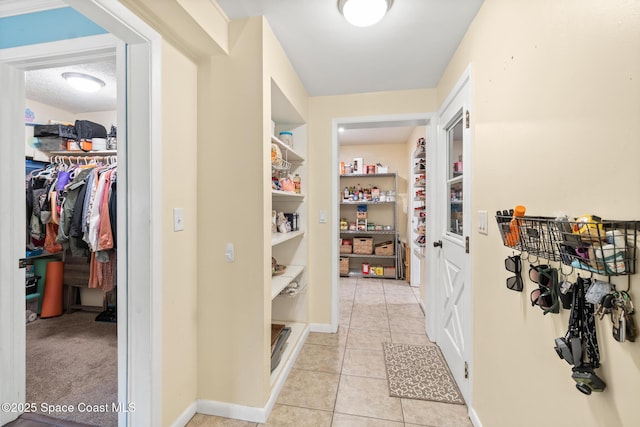 hallway featuring light tile patterned floors, baseboards, and a textured ceiling