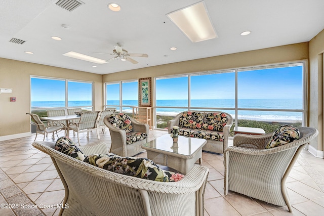 living room with a view of the beach, light tile patterned floors, ceiling fan, and a water view