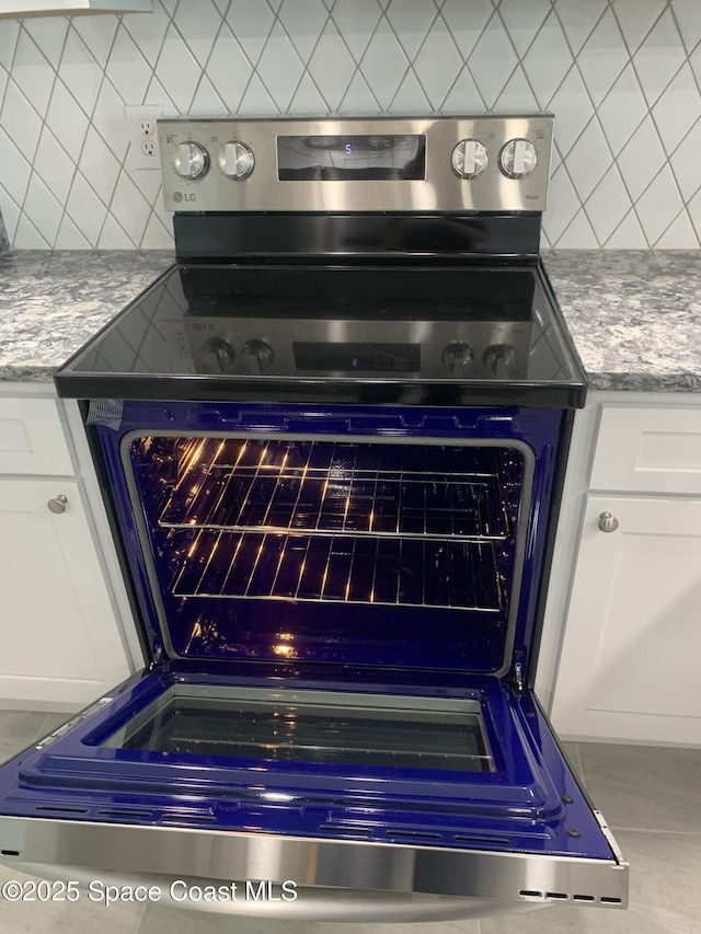 details featuring white cabinetry, light stone counters, stainless steel range with electric cooktop, and backsplash