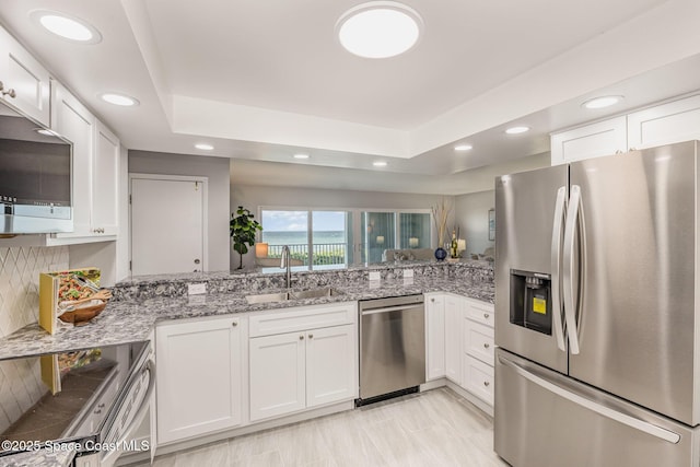 kitchen featuring appliances with stainless steel finishes, sink, white cabinets, and a tray ceiling