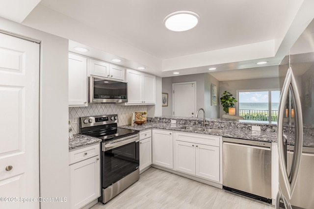 kitchen with sink, white cabinetry, appliances with stainless steel finishes, light stone countertops, and decorative backsplash