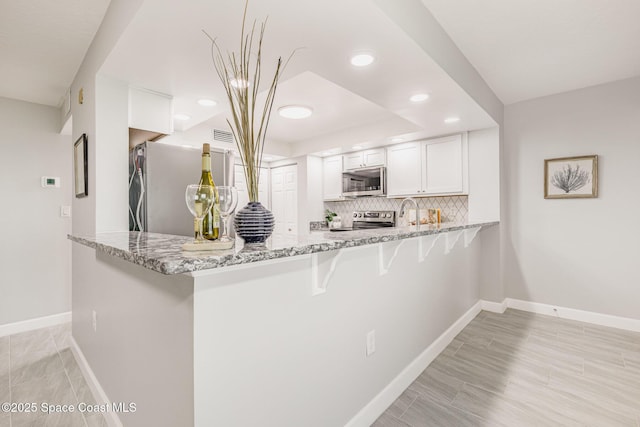 kitchen featuring light stone counters, kitchen peninsula, white cabinets, stainless steel appliances, and backsplash