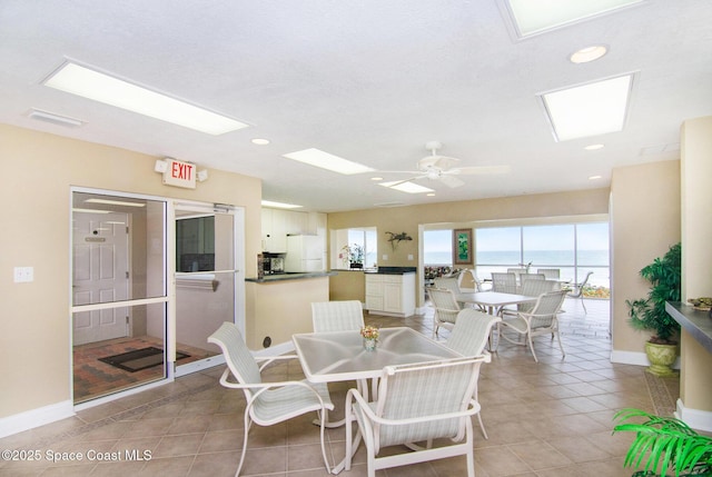 dining space featuring light tile patterned flooring, a water view, and ceiling fan