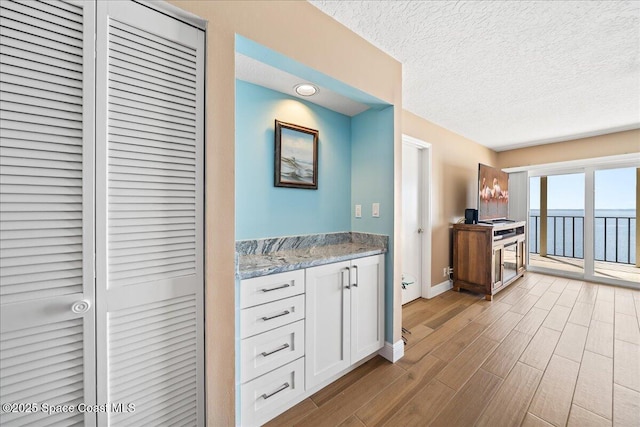 kitchen featuring light stone counters, light wood-type flooring, a textured ceiling, and white cabinets