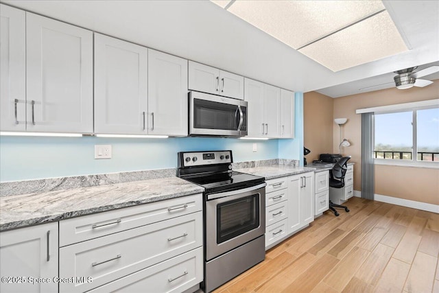 kitchen with white cabinetry, appliances with stainless steel finishes, light stone counters, and light hardwood / wood-style flooring