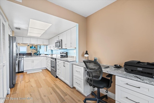 kitchen with light wood-type flooring, light stone countertops, white cabinets, and appliances with stainless steel finishes