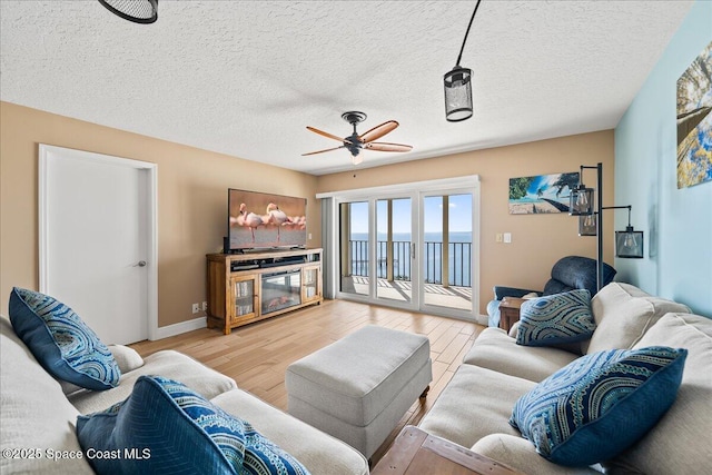 living room with ceiling fan, a fireplace, a textured ceiling, and light wood-type flooring