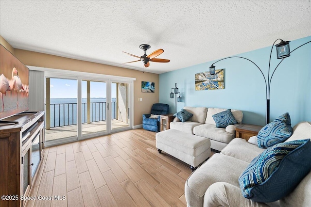 living room featuring ceiling fan, a water view, a textured ceiling, and light hardwood / wood-style flooring