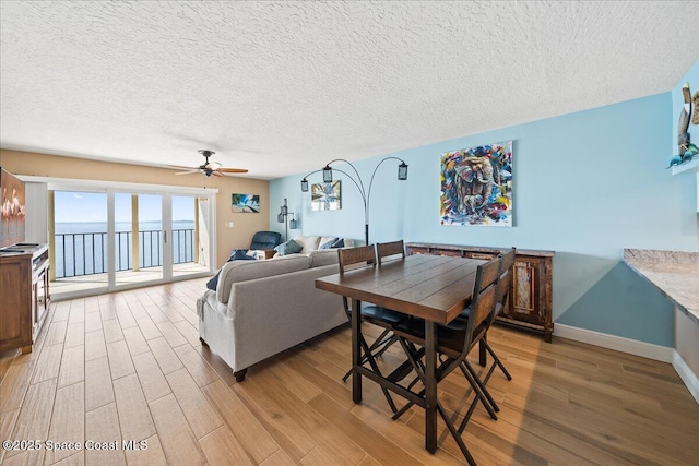 dining area featuring ceiling fan, a water view, hardwood / wood-style floors, and a textured ceiling