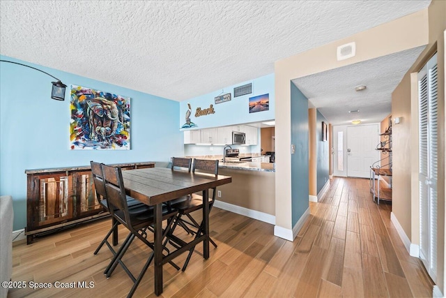 dining space featuring sink, light hardwood / wood-style flooring, and a textured ceiling