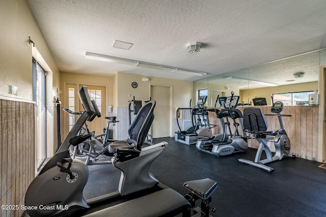 exercise room with wooden walls and a textured ceiling