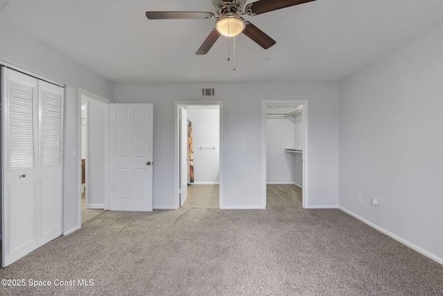 unfurnished bedroom featuring a spacious closet, light carpet, ceiling fan, and a closet