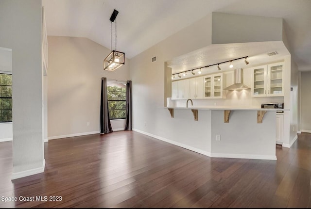 kitchen with wall chimney range hood, a breakfast bar area, white cabinetry, dark hardwood / wood-style floors, and kitchen peninsula