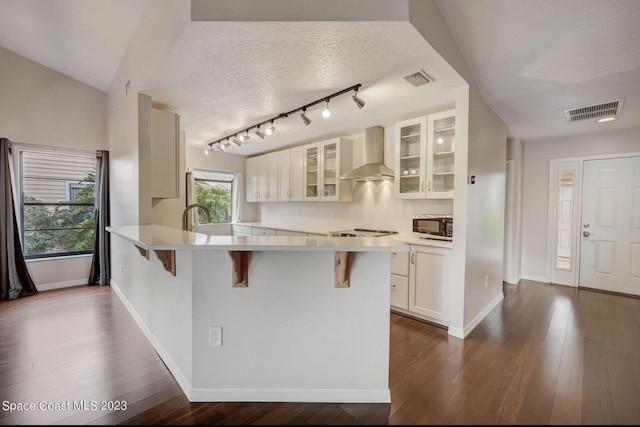 kitchen featuring white cabinetry, dark hardwood / wood-style flooring, a kitchen bar, and wall chimney exhaust hood