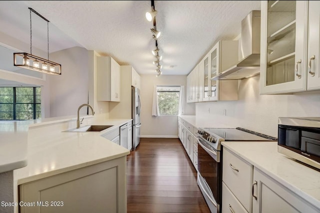 kitchen featuring appliances with stainless steel finishes, sink, hanging light fixtures, light stone counters, and wall chimney exhaust hood