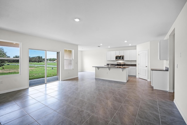 kitchen featuring tile patterned floors, a breakfast bar, stainless steel appliances, a kitchen island with sink, and white cabinets