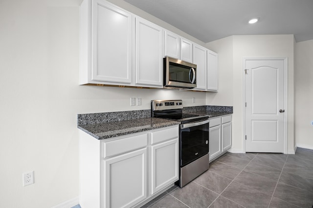 kitchen featuring white cabinetry, stainless steel appliances, light tile patterned flooring, and dark stone countertops