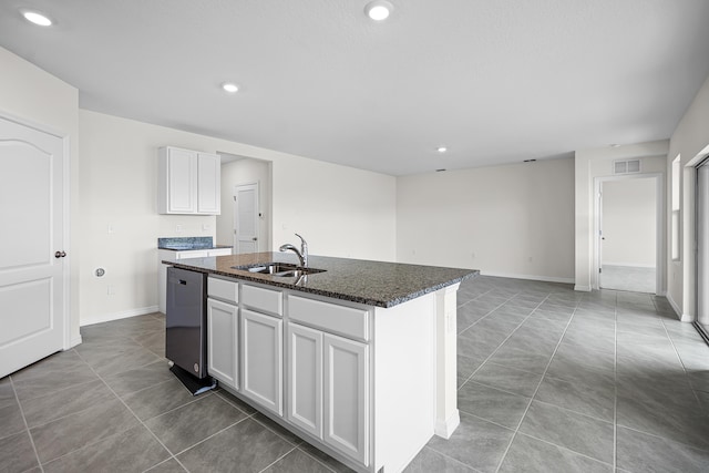 kitchen featuring an island with sink, sink, dark stone countertops, white cabinets, and stainless steel dishwasher