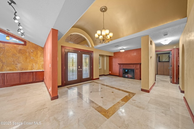 foyer featuring track lighting, a textured ceiling, vaulted ceiling, french doors, and a chandelier