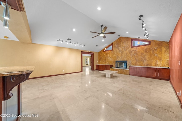 unfurnished living room featuring rail lighting, lofted ceiling, ceiling fan, and a fireplace