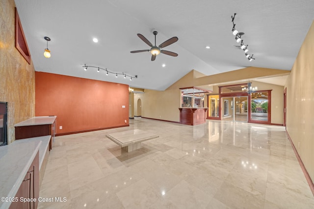 interior space with ceiling fan with notable chandelier, track lighting, a fireplace, and vaulted ceiling