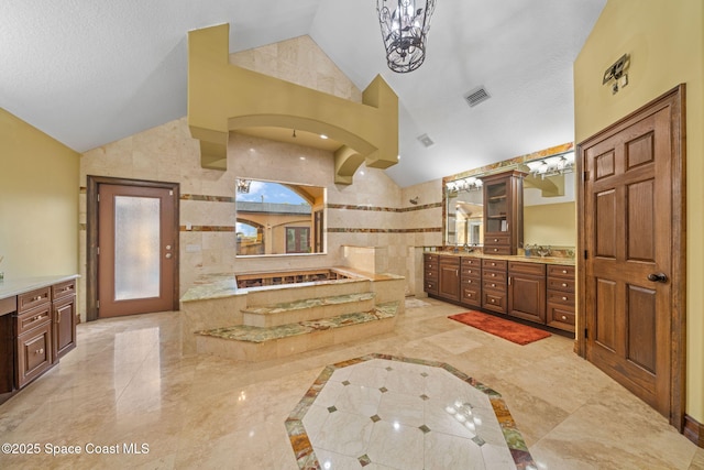 bathroom with tiled tub, tile walls, vanity, a textured ceiling, and vaulted ceiling